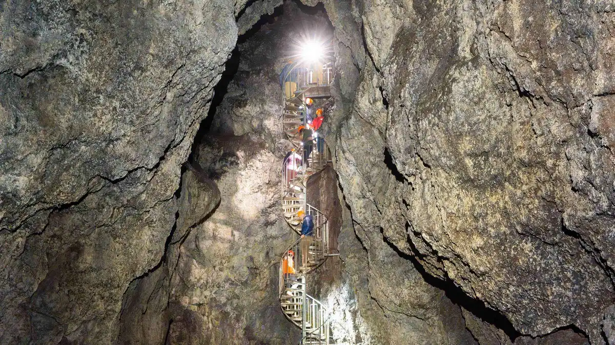 Guided group with helmets and torches on the spiral staircase inside the Vatnshellir lava cave on the Snæfellsnes peninsula in Iceland